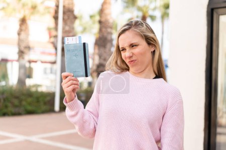 Photo for Young blonde woman holding a passport at outdoors with sad expression - Royalty Free Image