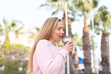 Foto de Joven mujer rubia sosteniendo un café para llevar al aire libre - Imagen libre de derechos