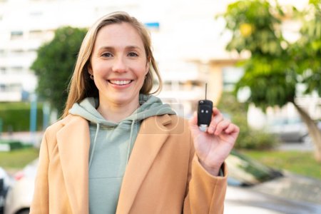 Téléchargez les photos : Jeune femme blonde tenant des clés de voiture à l'extérieur souriant beaucoup - en image libre de droit