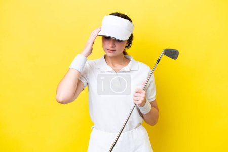 Téléchargez les photos : Jeune femme caucasienne jouer au golf isolé sur fond jaune avec mal de tête - en image libre de droit