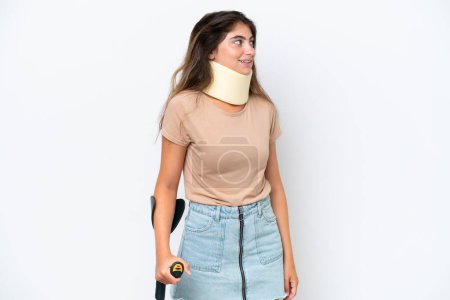 Photo for Young caucasian woman wearing neck brace and crutch isolated on white background looking side - Royalty Free Image