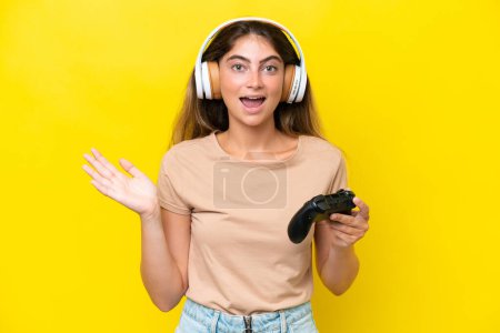 Téléchargez les photos : Jeune femme caucasienne jouant avec un contrôleur de jeu vidéo isolé sur fond jaune avec expression faciale choquée - en image libre de droit