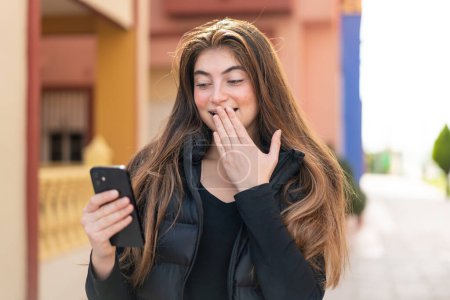 Téléchargez les photos : Jeune jolie femme caucasienne utilisant un téléphone mobile à l'extérieur avec une expression faciale surprise et choquée - en image libre de droit