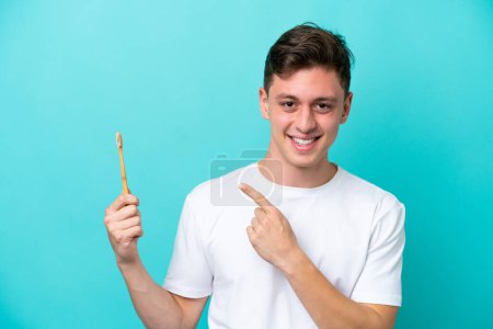 Téléchargez les photos : Jeune homme brésilien brossant des dents isolées sur fond bleu pointant vers le côté pour présenter un produit - en image libre de droit