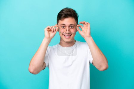 Foto de Young handsome Brazilian man isolated on blue background With glasses with happy expression - Imagen libre de derechos