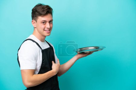 Photo for Young waitress with tray isolated on blue background pointing back - Royalty Free Image