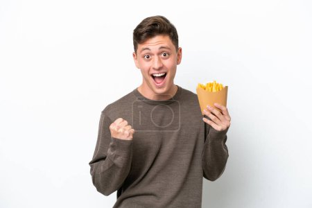 Photo for Young Brazilian man holding fried chips isolated on white background celebrating a victory in winner position - Royalty Free Image
