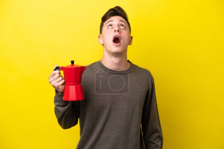 Photo for Young Brazilian man holding coffee pot isolated on yellow background looking up and with surprised expression - Royalty Free Image