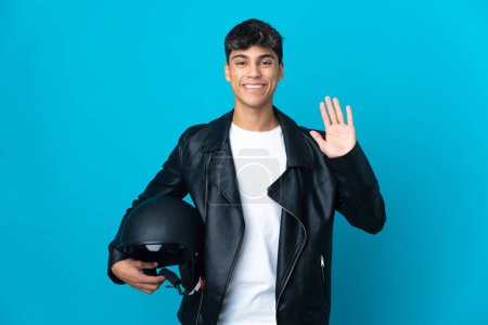 Photo for Young man with a motorcycle helmet over isolated blue background saluting with hand with happy expression - Royalty Free Image