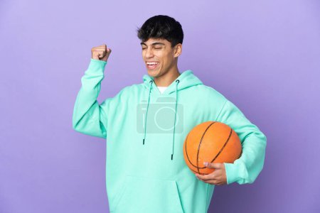 Foto de Joven jugando baloncesto sobre fondo púrpura aislado celebrando una victoria - Imagen libre de derechos