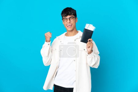 Téléchargez les photos : Jeune homme sur fond bleu isolé heureux en vacances avec passeport et billets d'avion - en image libre de droit