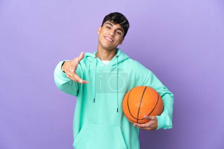 Téléchargez les photos : Jeune homme jouant au basket sur fond violet isolé serrant la main pour conclure une bonne affaire - en image libre de droit