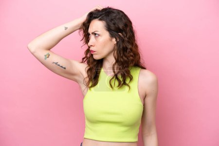 Photo for Young caucasian woman isolated on pink background having doubts while scratching head - Royalty Free Image