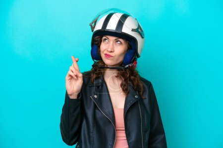 Foto de Mujer joven caucásica con un casco de moto aislado sobre fondo azul con los dedos cruzando y deseando lo mejor - Imagen libre de derechos