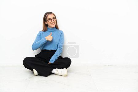 Foto de Joven mujer caucásica sentada en el suelo dando un gesto de pulgares hacia arriba - Imagen libre de derechos