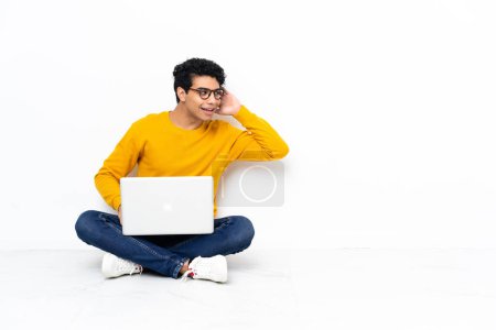 Photo for Venezuelan man sitting on the floor with laptop listening to something by putting hand on the ear - Royalty Free Image