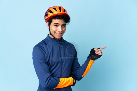 Foto de Hombre ciclista venezolano aislado sobre fondo azul apuntando con el dedo hacia un lado - Imagen libre de derechos