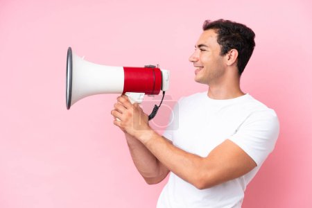 Téléchargez les photos : Jeune homme caucasien isolé sur fond rose criant à travers un mégaphone pour annoncer quelque chose - en image libre de droit