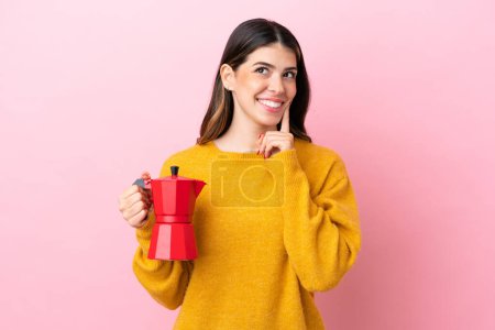 Téléchargez les photos : Young Italian woman holding a coffee maker isolated on pink background thinking an idea while looking up - en image libre de droit