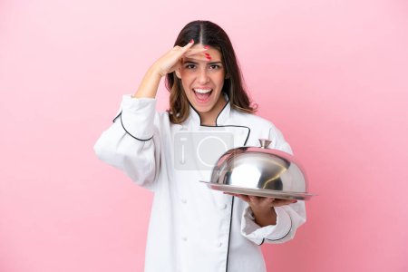 Photo for Young Italian chef woman holding tray with lid isolated on pink background doing surprise gesture while looking to the side - Royalty Free Image