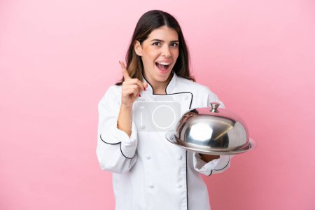 Foto de Young Italian chef woman holding tray with lid isolated on pink background intending to realizes the solution while lifting a finger up - Imagen libre de derechos