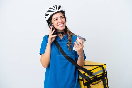 Téléchargez les photos : Young delivery woman with thermal backpack isolated on white background holding coffee to take away and a mobile - en image libre de droit