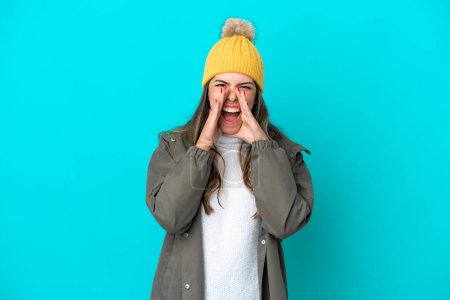 Photo for Young Italian woman wearing winter jacket and hat isolated on blue background shouting and announcing something - Royalty Free Image