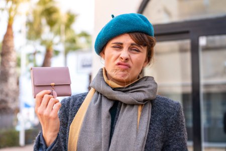 Foto de Mujer morena sosteniendo una billetera al aire libre con expresión triste - Imagen libre de derechos