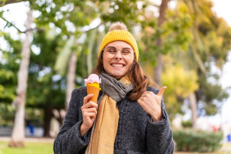 Foto de Mujer morena con un helado de corneta al aire libre apuntando a un lado para presentar un producto - Imagen libre de derechos