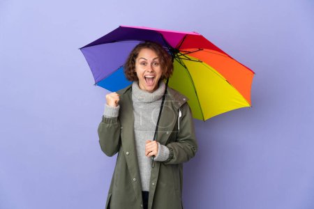 Foto de Mujer inglesa sosteniendo un paraguas aislado sobre fondo púrpura celebrando una victoria en posición ganadora - Imagen libre de derechos