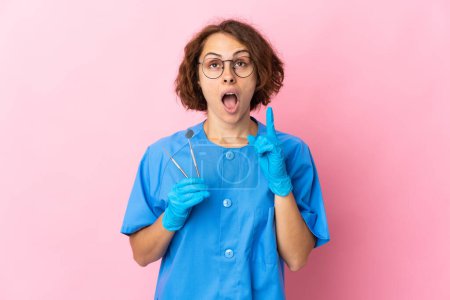 Téléchargez les photos : Femme dentiste anglais tenant des outils sur isolé sur fond rose pensant une idée pointant le doigt vers le haut - en image libre de droit