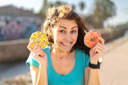 Photo for Young sport woman at outdoors holding donuts - Royalty Free Image