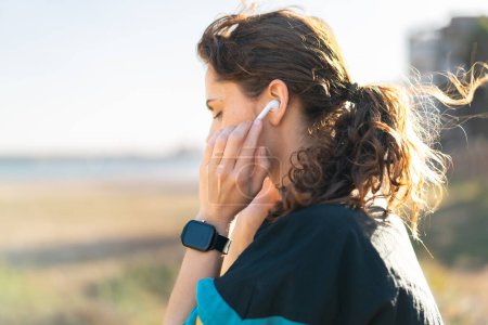Téléchargez les photos : Jeune femme à l'extérieur portant des vêtements de sport et écoutant de la musique avec des écouteurs sans fil - en image libre de droit