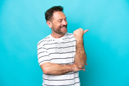 Foto de Middle age caucasian man isolated on blue background pointing to the side to present a product - Imagen libre de derechos