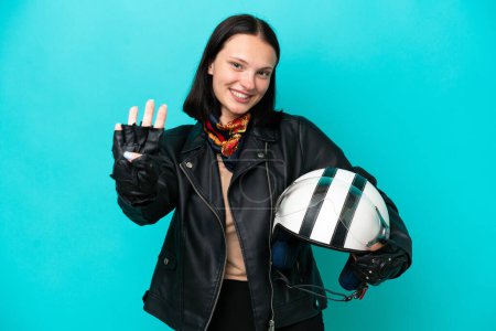 Foto de Joven mujer caucásica con un casco de moto aislado sobre fondo azul feliz y contando cuatro con los dedos - Imagen libre de derechos