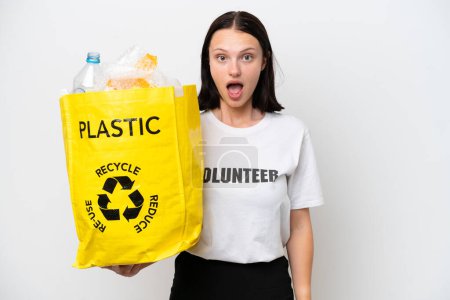 Foto de Mujer caucásica joven sosteniendo una bolsa llena de botellas de plástico para reciclar aislado sobre fondo blanco con expresión facial sorpresa - Imagen libre de derechos