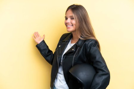 Téléchargez les photos : Jeune femme caucasienne avec un casque de moto isolé sur fond jaune étendant les mains sur le côté pour inviter à venir - en image libre de droit