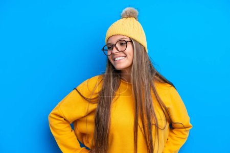 Photo for Young caucasian woman wearing winter clothes isolated on blue background posing with arms at hip and smiling - Royalty Free Image