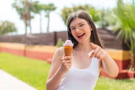 Foto de Joven mujer ucraniana bonita con un helado de corneta al aire libre apunta con el dedo a usted con una expresión de confianza - Imagen libre de derechos