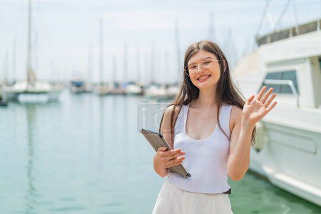 Photo for Young pretty Ukrainian woman holding a tablet at outdoors saluting with hand with happy expression - Royalty Free Image