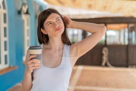 Téléchargez les photos : Jeune jolie femme ukrainienne tenant un café à emporter à l'extérieur ayant des doutes et avec une expression du visage confus - en image libre de droit