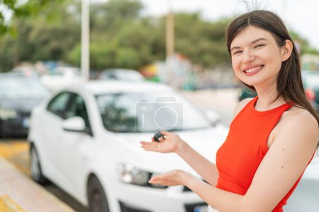 Téléchargez les photos : Jeune jolie femme à l'extérieur tenant des clés de voiture avec expression heureuse - en image libre de droit