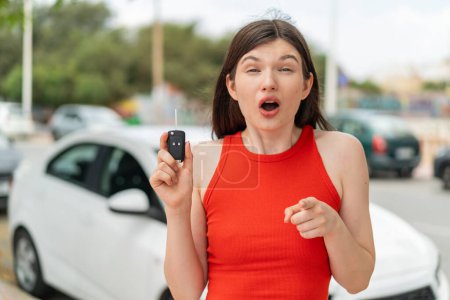 Photo for Young pretty Ukrainian woman holding car keys at outdoors surprised and pointing front - Royalty Free Image