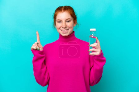 Téléchargez les photos : Jeune femme caucasienne rougeâtre avec une bouteille d'eau isolée sur fond bleu pointant vers le haut d'une grande idée - en image libre de droit
