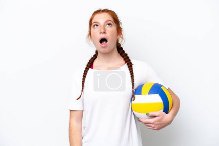 Foto de Joven mujer caucásica rojiza jugando voleibol aislado sobre fondo blanco mirando hacia arriba y con expresión sorprendida - Imagen libre de derechos