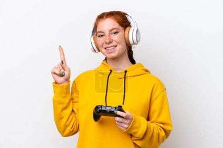 Téléchargez les photos : Jeune femme rougeâtre jouant avec un contrôleur de jeu vidéo isolé sur fond blanc montrant et levant un doigt en signe du meilleur - en image libre de droit