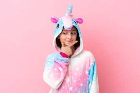 Foto de Pequeña mujer caucásica con un pijama de unicornio aislado sobre fondo rosa pensando - Imagen libre de derechos