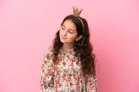 Foto de Pequeña princesa caucásica con corona aislada sobre fondo rosa mirando hacia un lado y sonriendo - Imagen libre de derechos