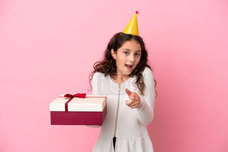 Photo for Little caucasian girl holding a gift isolated on pink background surprised and pointing front - Royalty Free Image