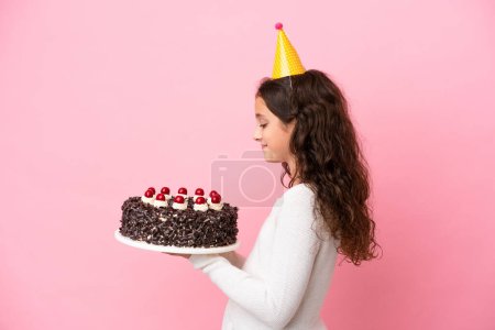 Téléchargez les photos : Petite fille caucasienne tenant gâteau d'anniversaire isolé sur fond rose avec expression heureuse - en image libre de droit